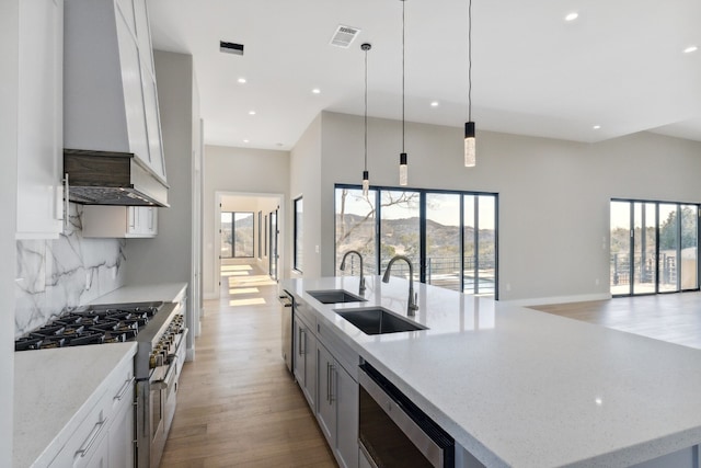 kitchen featuring stainless steel appliances, decorative light fixtures, a center island with sink, light hardwood / wood-style floors, and white cabinetry