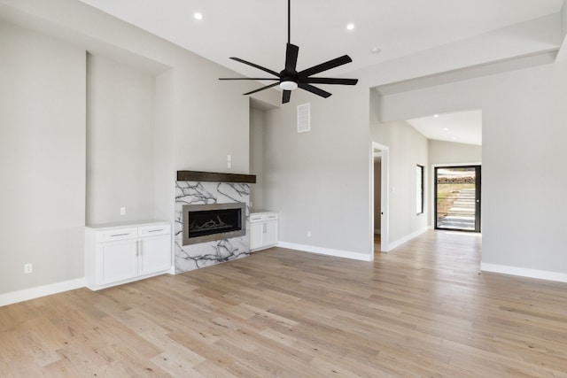 unfurnished living room with a premium fireplace, ceiling fan, vaulted ceiling, and light wood-type flooring