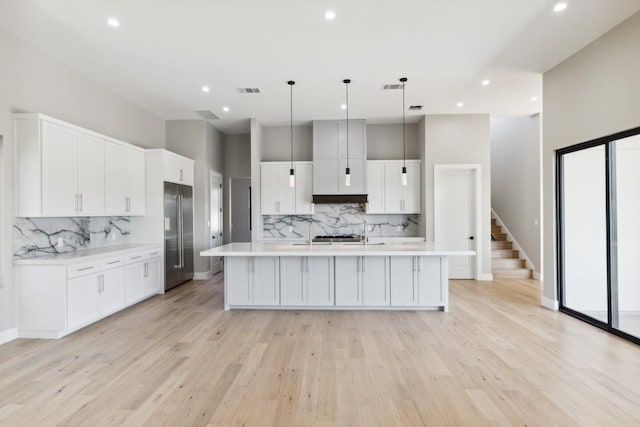 kitchen with decorative light fixtures, stainless steel built in fridge, a center island with sink, and light hardwood / wood-style flooring