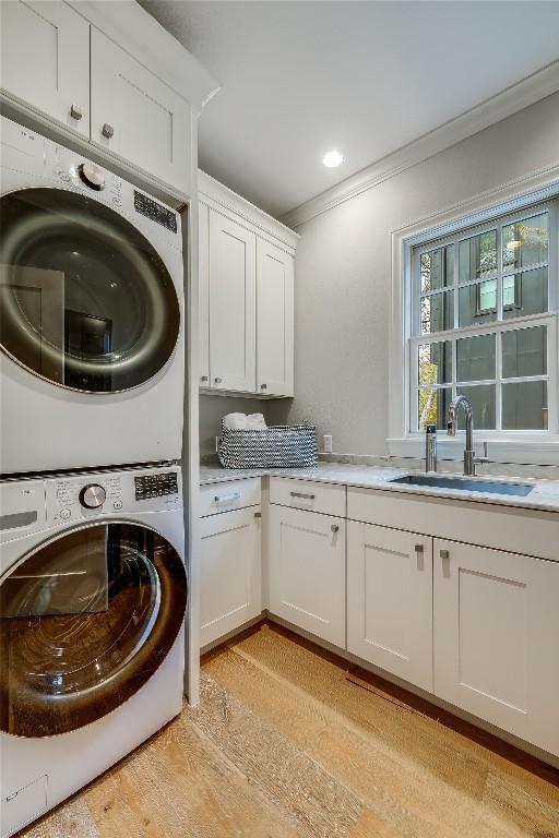 laundry room with cabinets, light wood-type flooring, crown molding, sink, and stacked washer and clothes dryer