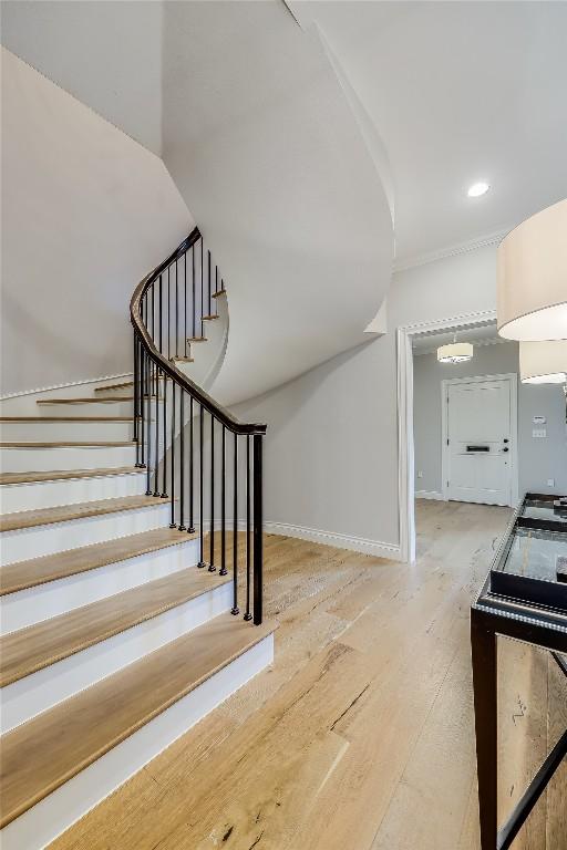 staircase with recessed lighting, wood finished floors, baseboards, and ornamental molding