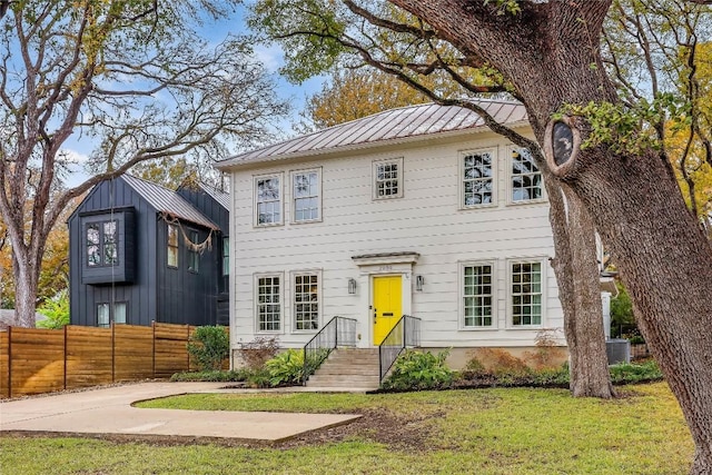 colonial home featuring a front lawn, a standing seam roof, metal roof, and fence