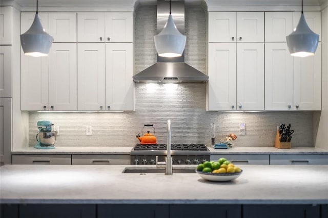 kitchen with wall chimney range hood, tasteful backsplash, a sink, and hanging light fixtures