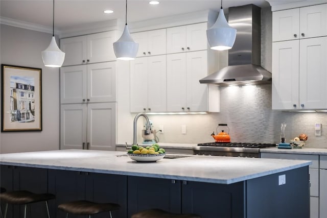 kitchen featuring crown molding, tasteful backsplash, a sink, a breakfast bar, and wall chimney exhaust hood