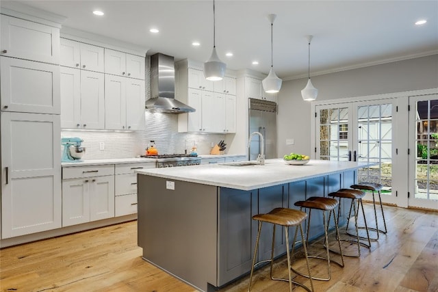 kitchen with white cabinets, wall chimney exhaust hood, sink, and an island with sink