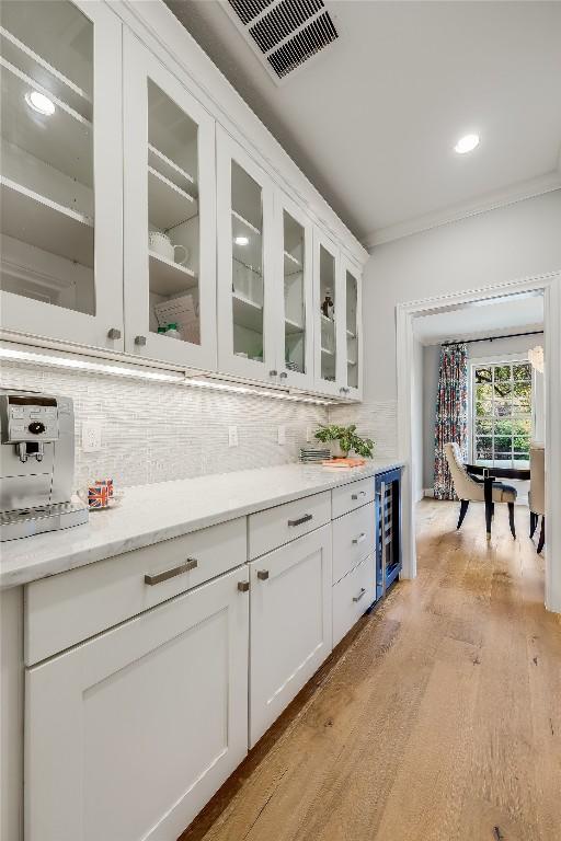 bar featuring light wood-type flooring, backsplash, light stone counters, white cabinetry, and wine cooler