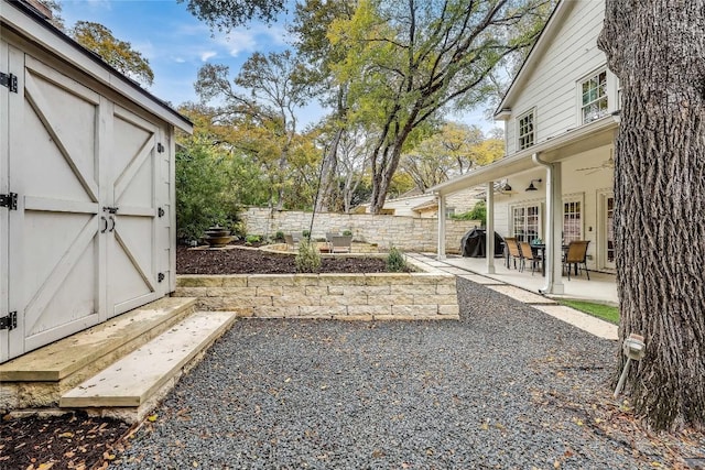 view of yard with a storage shed, an outbuilding, a fenced backyard, a patio area, and ceiling fan