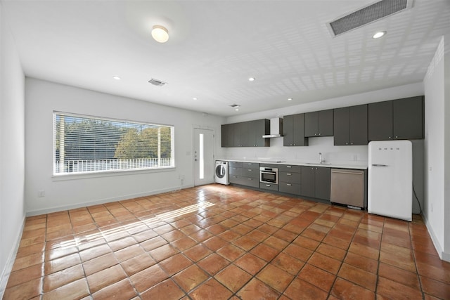 kitchen with sink, tile patterned flooring, wall chimney exhaust hood, washer / dryer, and stainless steel appliances