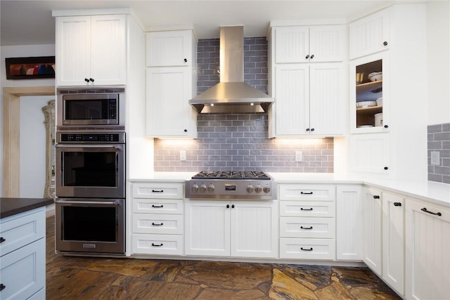 kitchen featuring decorative backsplash, white cabinetry, wall chimney range hood, and appliances with stainless steel finishes