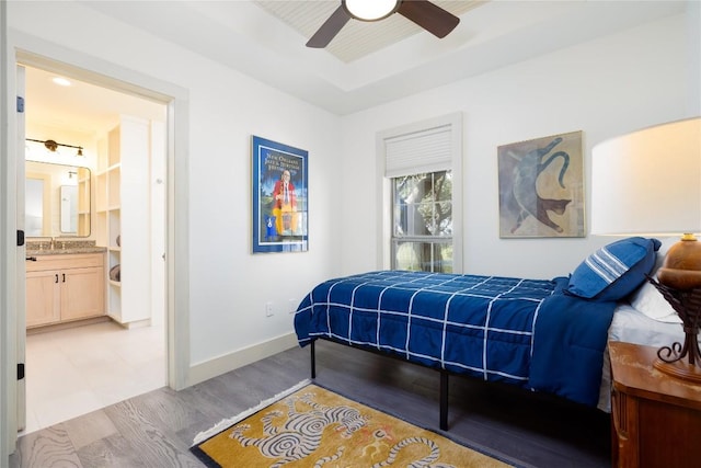 bedroom featuring light wood-type flooring, ensuite bath, ceiling fan, and sink