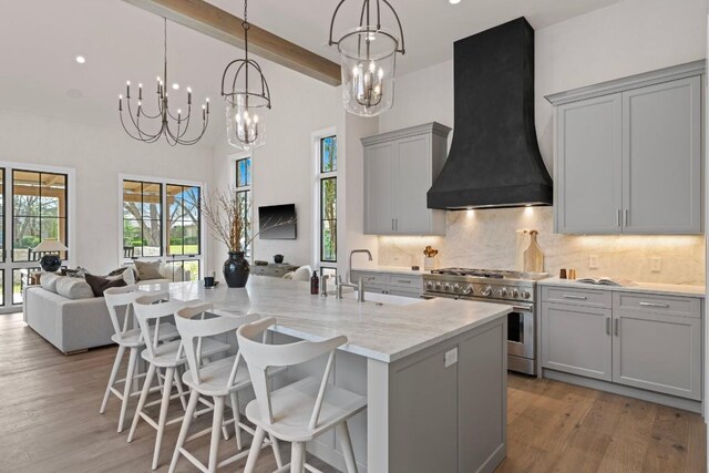 kitchen with light wood-type flooring, gray cabinetry, custom range hood, high end stove, and beam ceiling