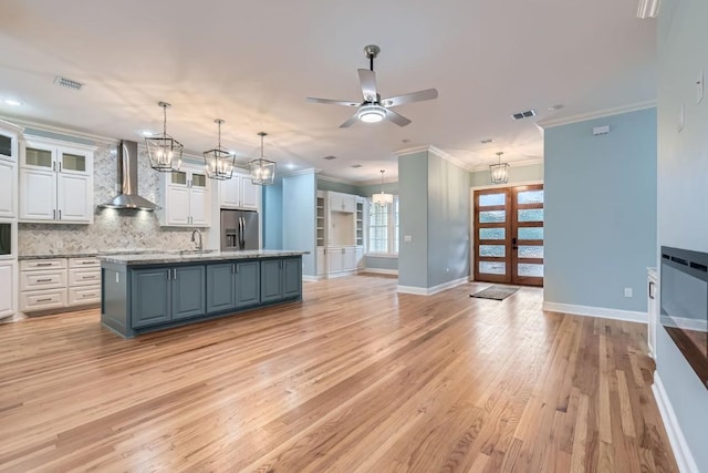 kitchen with stainless steel refrigerator with ice dispenser, white cabinetry, a kitchen island with sink, and wall chimney range hood