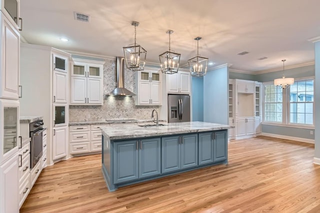 kitchen with wall chimney exhaust hood, stainless steel fridge with ice dispenser, pendant lighting, a center island with sink, and white cabinets