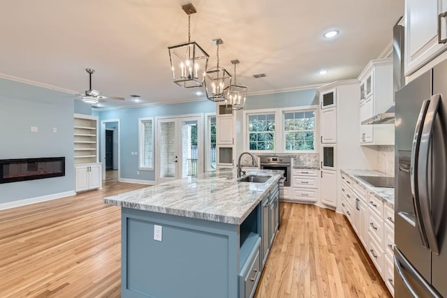 kitchen with white cabinets, light wood-type flooring, an island with sink, appliances with stainless steel finishes, and decorative light fixtures