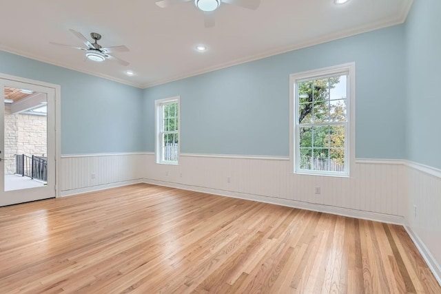 spare room featuring ceiling fan, a stone fireplace, light wood-type flooring, and crown molding