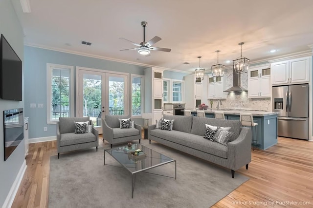 living room with french doors, ceiling fan with notable chandelier, sink, light wood-type flooring, and ornamental molding