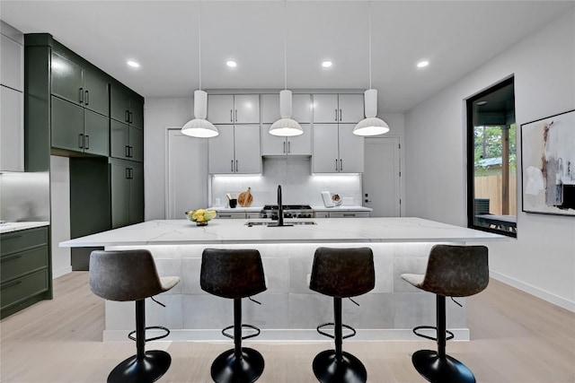 kitchen with decorative light fixtures, light stone counters, green cabinets, and sink