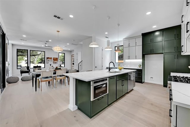 kitchen featuring sink, light stone counters, pendant lighting, a kitchen island with sink, and green cabinetry