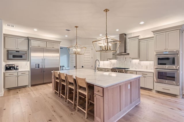 kitchen with stainless steel appliances, wall chimney range hood, a kitchen breakfast bar, light stone counters, and a spacious island