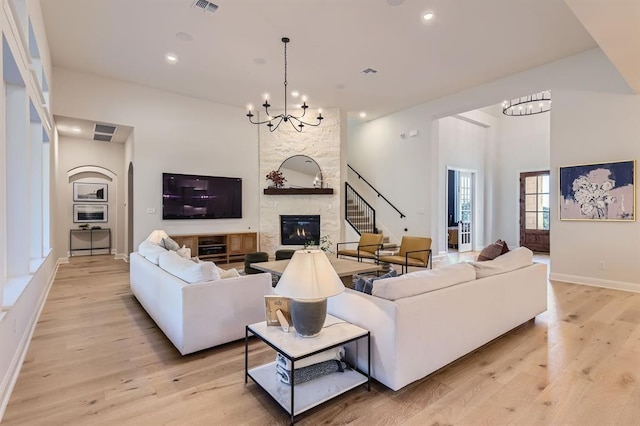 living room featuring a fireplace, light hardwood / wood-style flooring, a high ceiling, and a chandelier