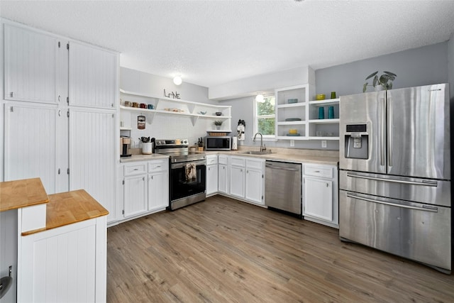 kitchen with sink, wood-type flooring, a textured ceiling, white cabinets, and appliances with stainless steel finishes