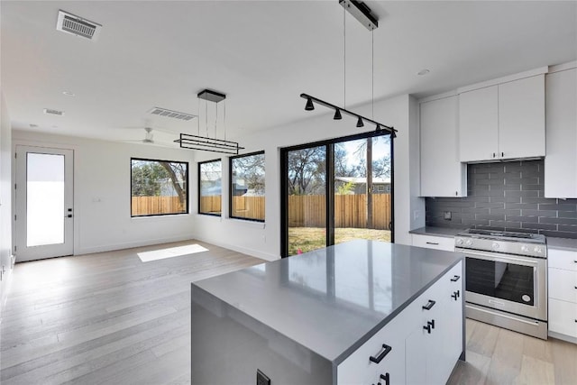 kitchen with stainless steel gas range oven, visible vents, backsplash, and light wood-style floors