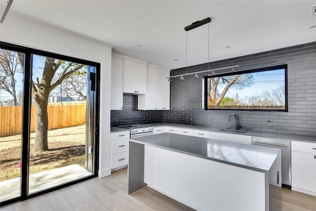 kitchen featuring a kitchen island, a sink, white cabinets, dishwasher, and tasteful backsplash