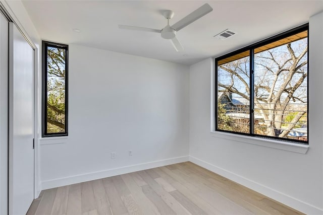 unfurnished room with visible vents, light wood-style flooring, a ceiling fan, and baseboards