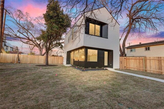 back of house at dusk featuring a lawn and a fenced backyard