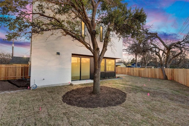 back of property at dusk with a fenced backyard and a lawn