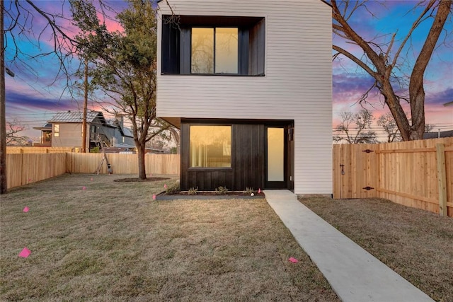 back of property at dusk with a yard and a fenced backyard