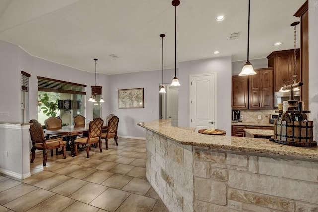 kitchen with decorative light fixtures, light stone counters, light tile patterned floors, and backsplash