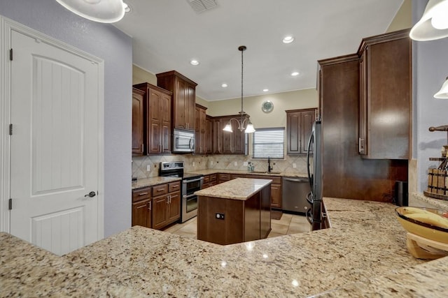 kitchen with a center island, stainless steel appliances, tasteful backsplash, light stone counters, and decorative light fixtures