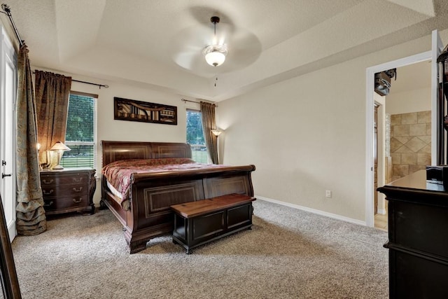 bedroom featuring a tray ceiling, ceiling fan, ensuite bathroom, and light colored carpet