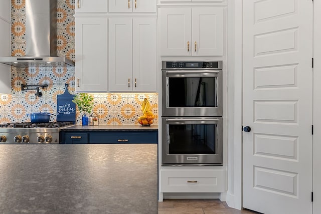 kitchen featuring tasteful backsplash, white cabinets, appliances with stainless steel finishes, and wall chimney exhaust hood