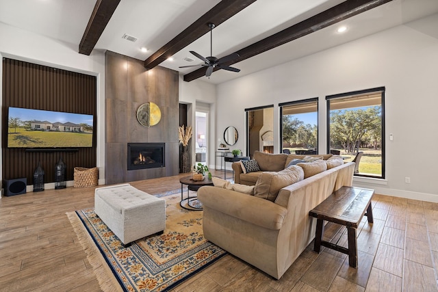 living room featuring ceiling fan, beamed ceiling, and a fireplace