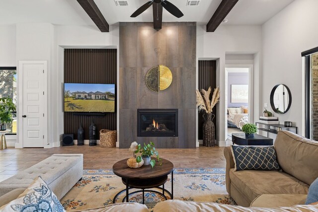 living room featuring ceiling fan, beam ceiling, light wood-type flooring, and a fireplace