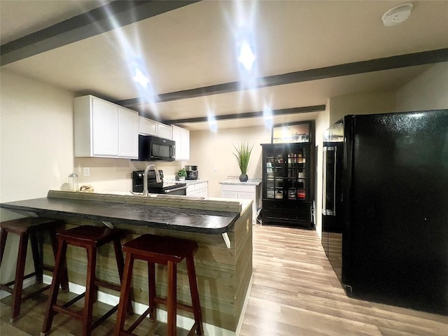 kitchen featuring kitchen peninsula, a breakfast bar, white cabinets, black appliances, and light wood-type flooring