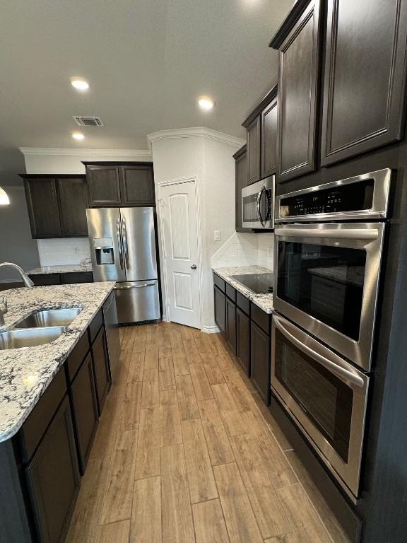 kitchen with sink, stainless steel appliances, light stone counters, light hardwood / wood-style flooring, and dark brown cabinets