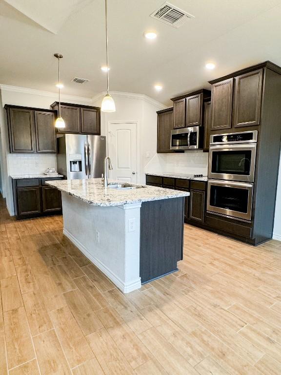 kitchen featuring a kitchen island with sink, hanging light fixtures, light wood-type flooring, appliances with stainless steel finishes, and dark brown cabinets