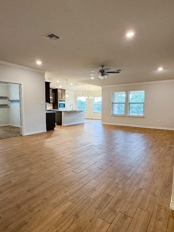 unfurnished living room featuring light hardwood / wood-style floors, ceiling fan, crown molding, and sink