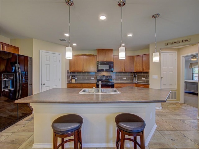 kitchen featuring a kitchen breakfast bar, a kitchen island with sink, sink, black appliances, and pendant lighting