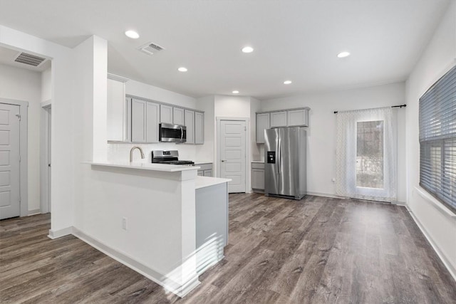 kitchen featuring sink, dark hardwood / wood-style flooring, kitchen peninsula, gray cabinets, and appliances with stainless steel finishes