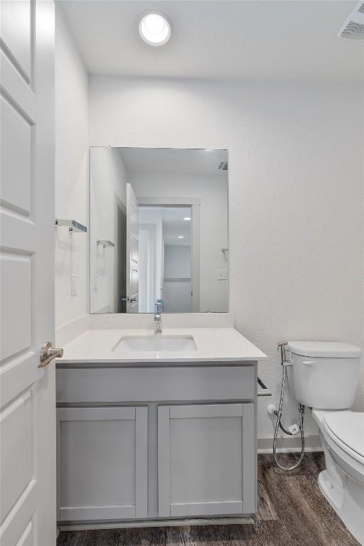 10400 Fulton Ave, Austin, TX 78754 - half bathroom featuring toilet, wood finished floors, vanity, and baseboards