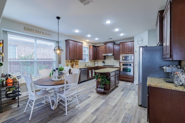 kitchen featuring appliances with stainless steel finishes, decorative backsplash, hanging light fixtures, light stone counters, and light hardwood / wood-style floors