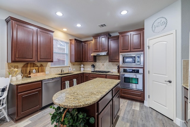 kitchen featuring sink, light wood-type flooring, a kitchen island, stainless steel appliances, and decorative backsplash