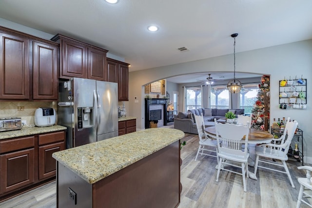 kitchen with a center island, stainless steel refrigerator with ice dispenser, tasteful backsplash, decorative light fixtures, and light wood-type flooring