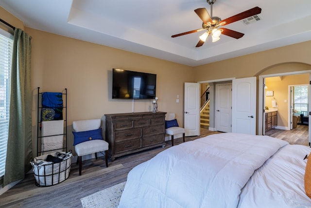 bedroom with visible vents, a raised ceiling, arched walkways, and wood finished floors