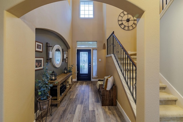 entryway with stairs, a high ceiling, wood finished floors, and baseboards