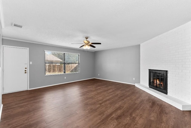 unfurnished living room featuring ceiling fan, dark hardwood / wood-style flooring, a textured ceiling, and a brick fireplace